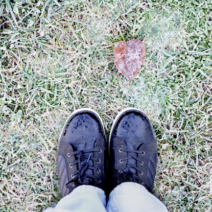 Feet in black boots and blue jeans on the grass covered with frost 