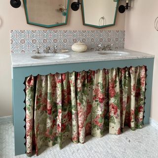 A bathroom with two mirrors and a floral curtain covering under-sink storage space