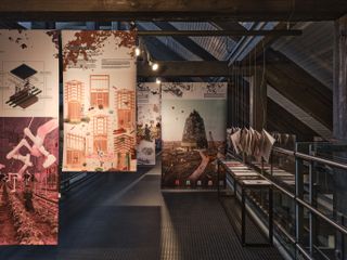 Interior view of the food and architecture exhibition panels at tallinn architecture biennale 2022, dark wood ceiling beams, arched glass skylight windows, silver handrail, black flooring, lighting
