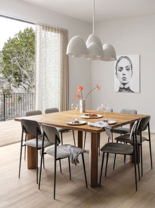 dining room with pale wood square table and floor and white walls and white feature light