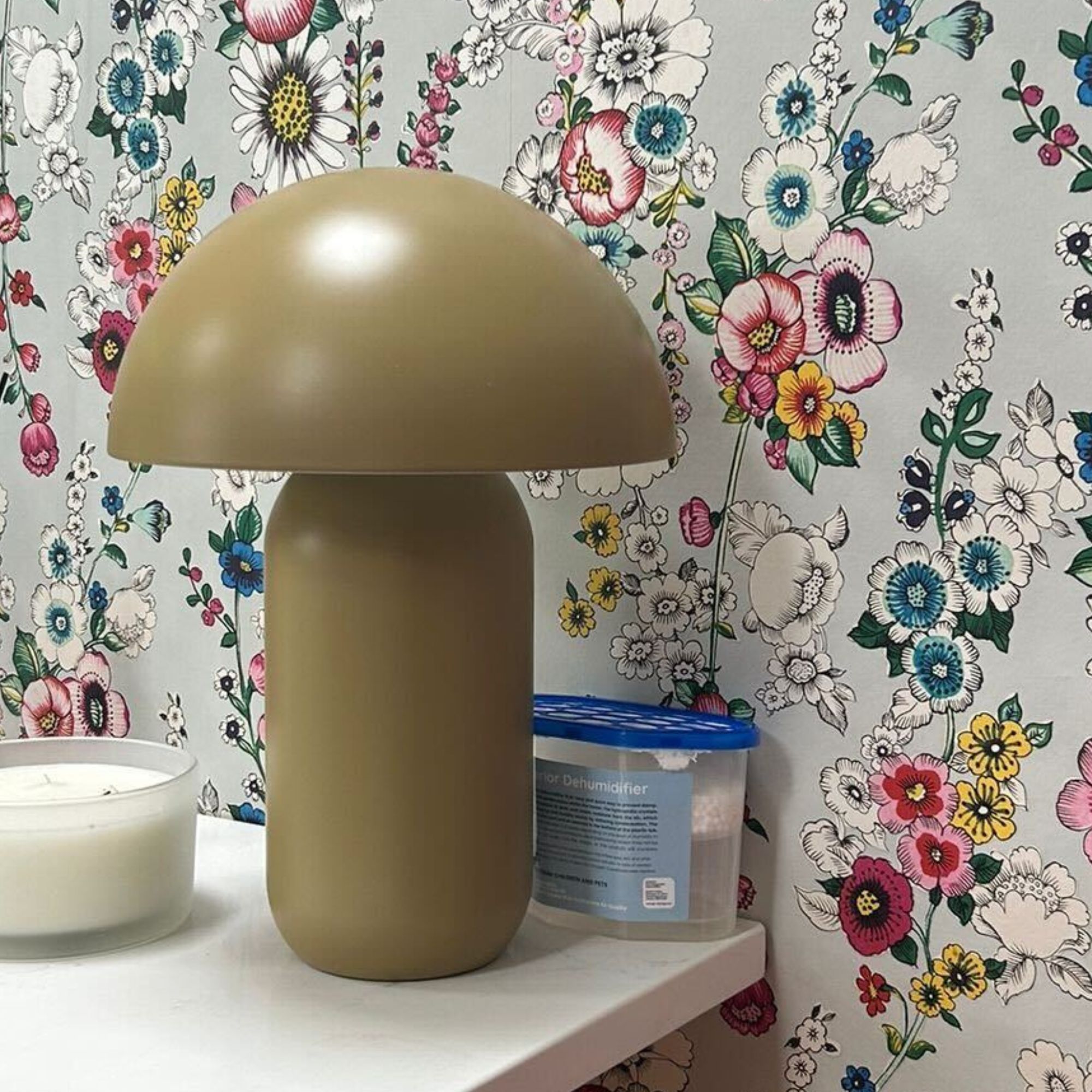A disposable dehumidifier behind a lamp against a bright floral wallpaper