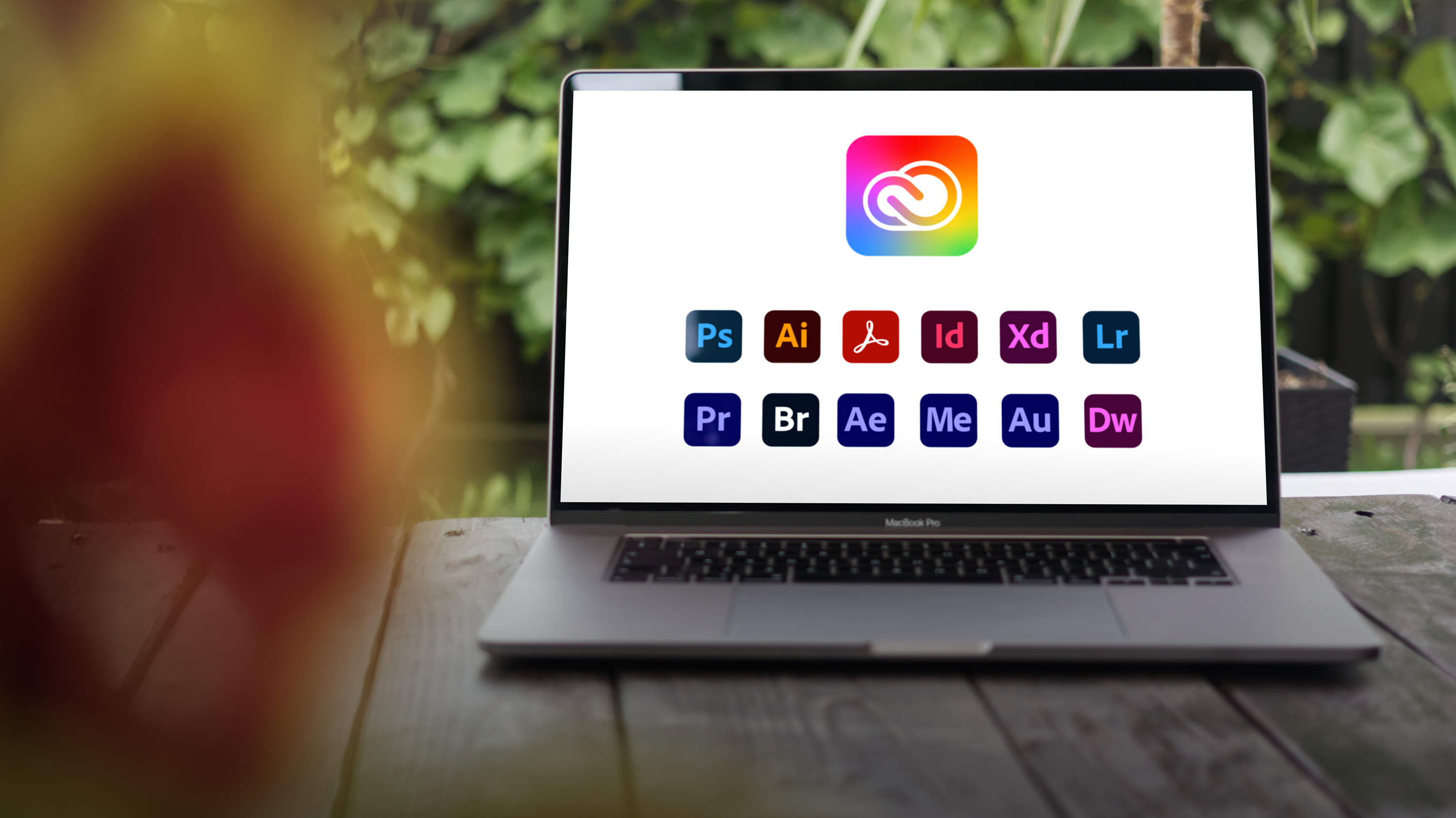 A laptop sits on a tabletop with the icons for the Adobe Creative Cloud All Apps plan on the screen