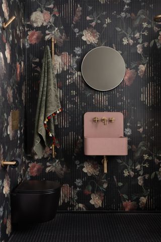 powder room with black floral wallpaper, black floor tiles, round mirror, towel hook, pink basin