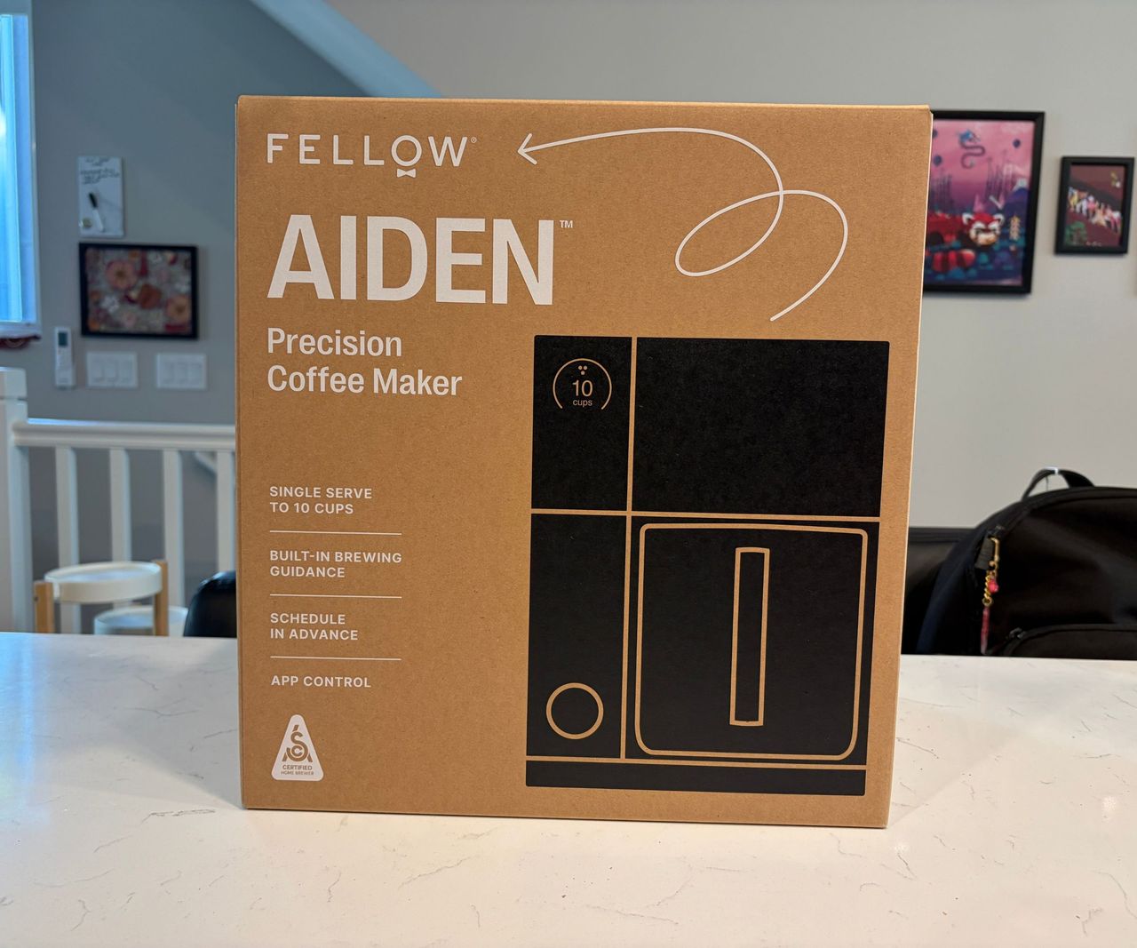 A brown cardboard box on a white kitchen counter with a black coffee maker printed on the front.