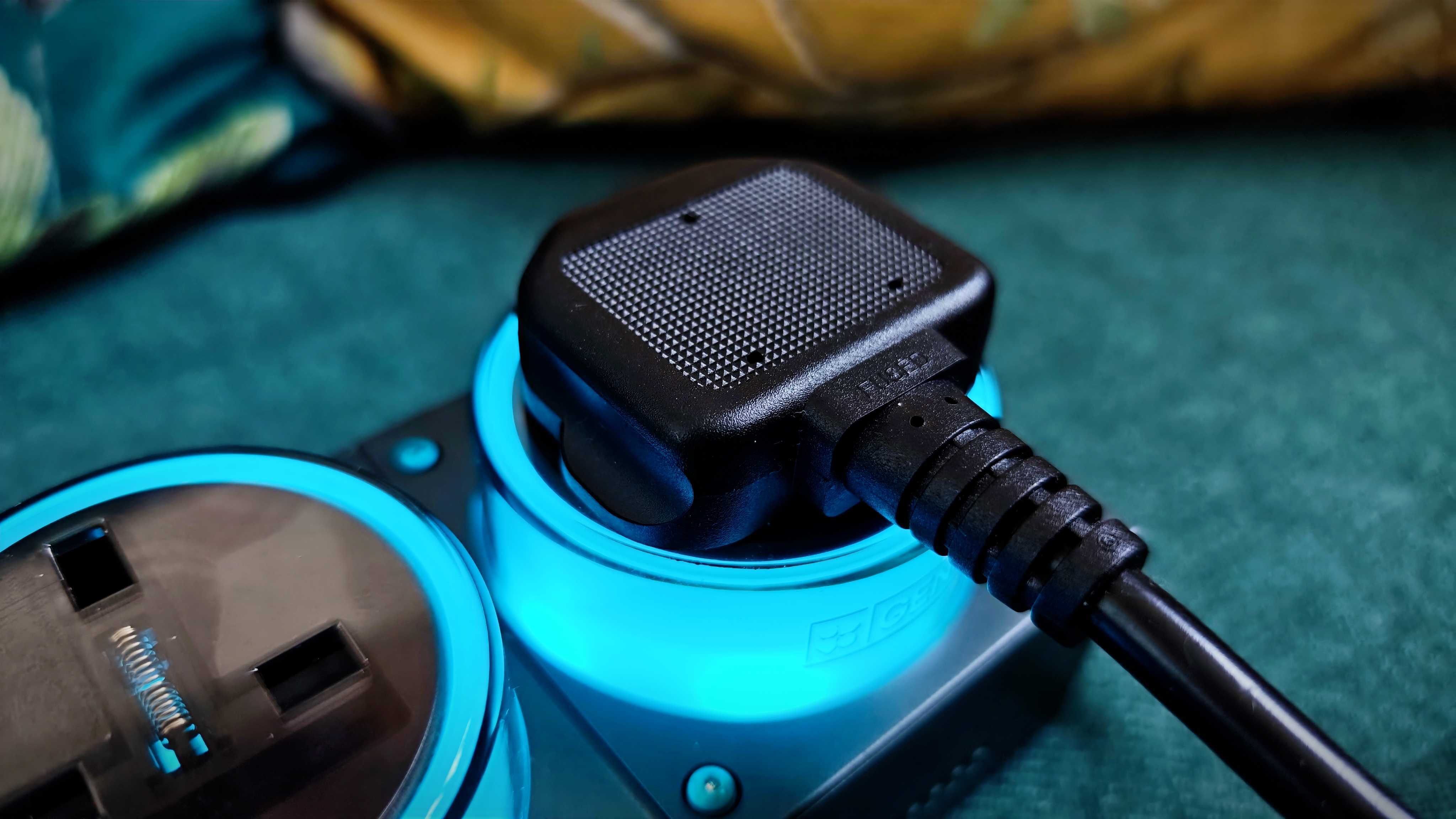 A grey-and-blue Genki Moonbase power strip and charging station sitting on a green sofa