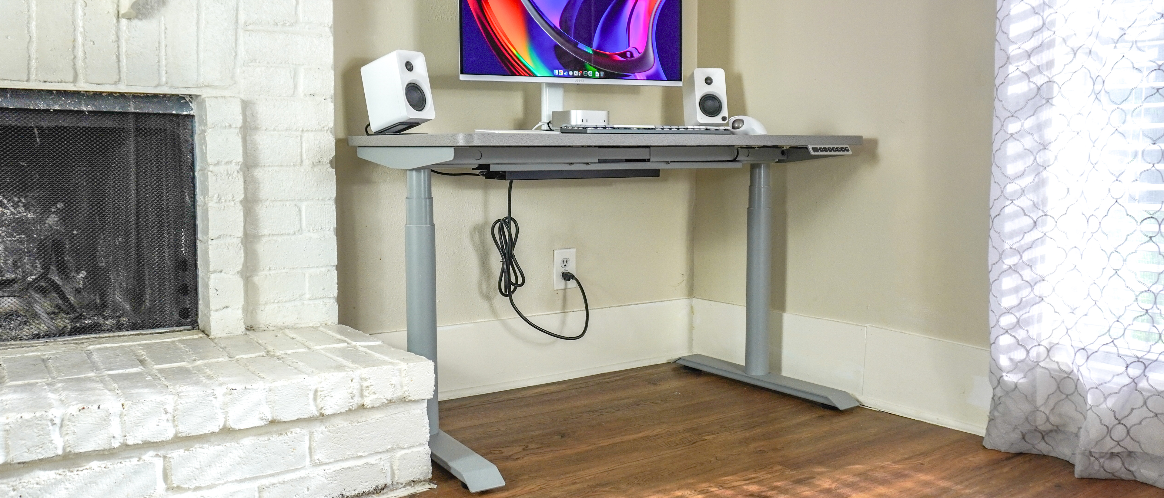 The Hinomi S1 standing desk set up in a corner next to a fireplace