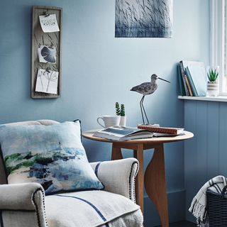 blue wall room with grey armchair with cushion and wooden round table bird object