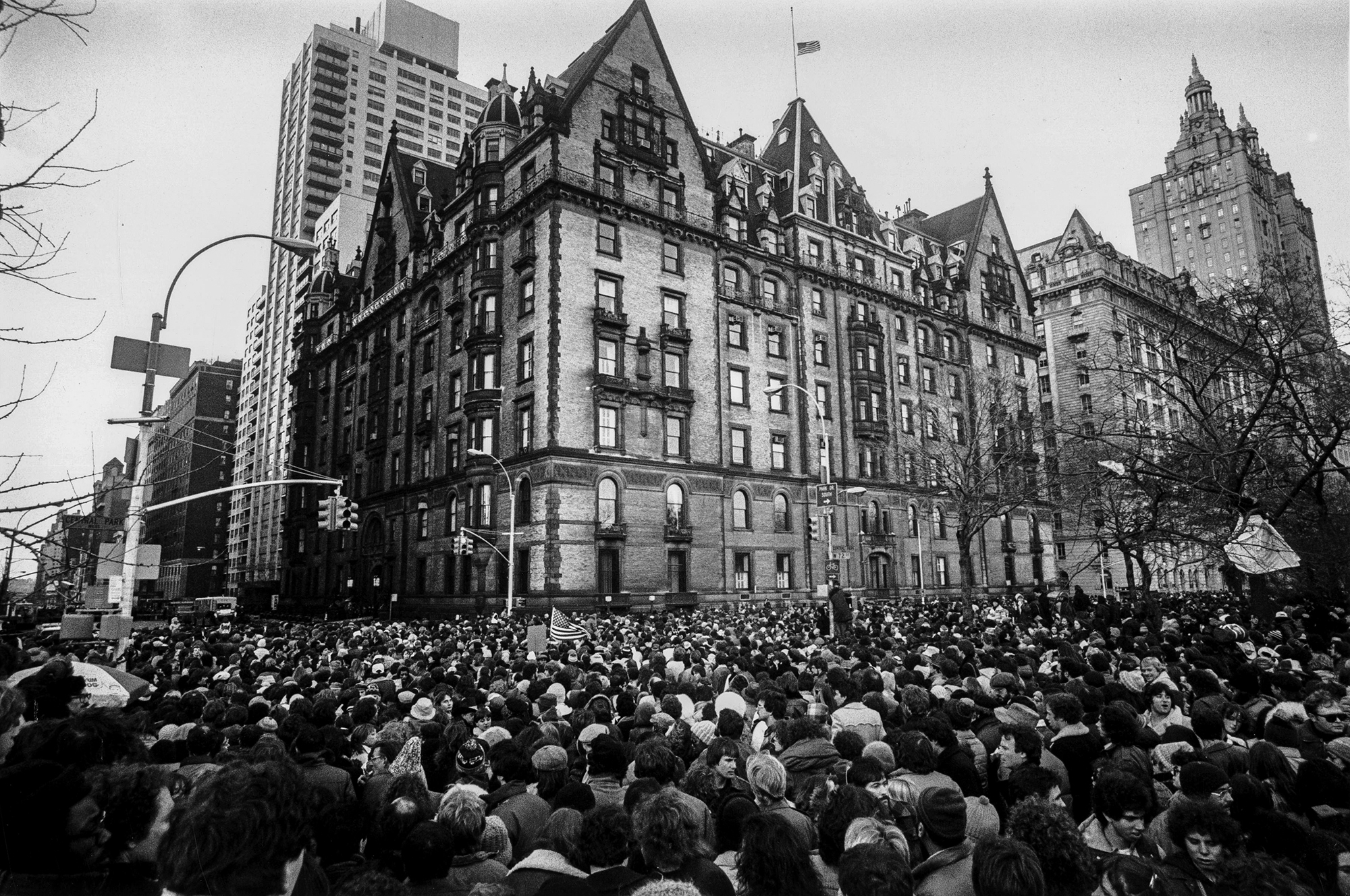 Crowds gathering outside the home of John Lennon in New York on December 9 19980, after the news that he had been shot and killed. A flag flies at half-mast over the building.