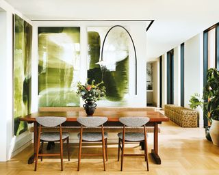 Modern, open-plan dining room with green artwork, curved wall lamp, wooden dining table, wooden floor