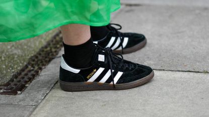  A guest wears a green short puffy sleeves / long midi dress, black socks, black suede with white leather logo sneakers from Adidas, outside 16Arlington, during London Fashion Week February 2023 on February 18, 2023 in London, England