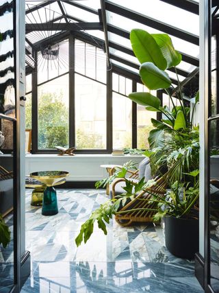 onservatory with dark grey frames, grey marbled floor and lush foliaged plants. Renovation of a Victorian terraced house in North West London, by interior designers Federica Gosio and Arianna Crosetta, home of Milly O'Sullivan.