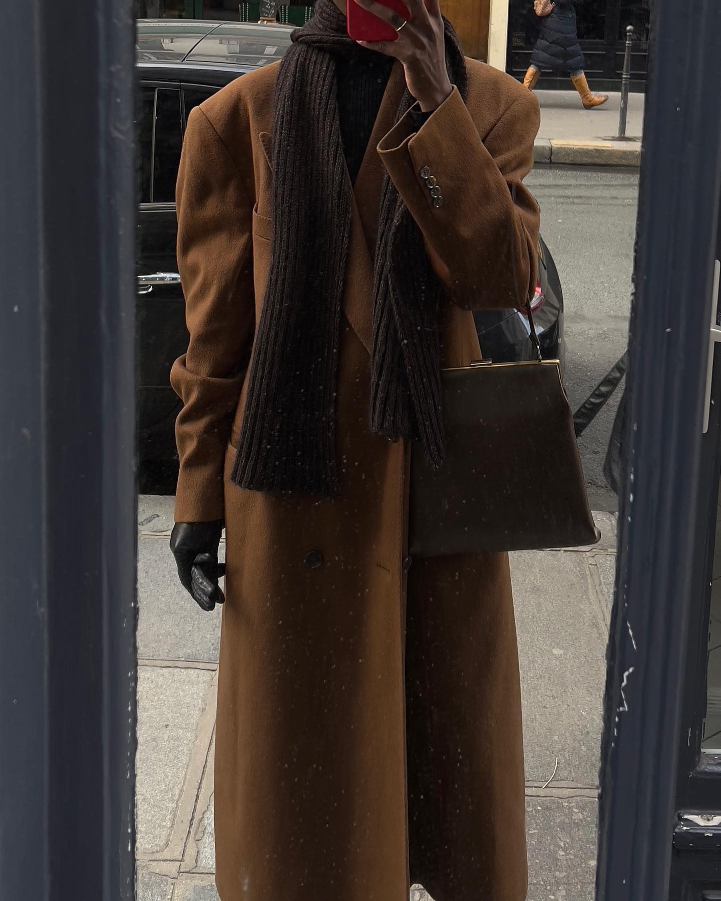 Sylvie Mus wearing a chestnut brown coat with a chocolate brown scarf and kisslock bag.