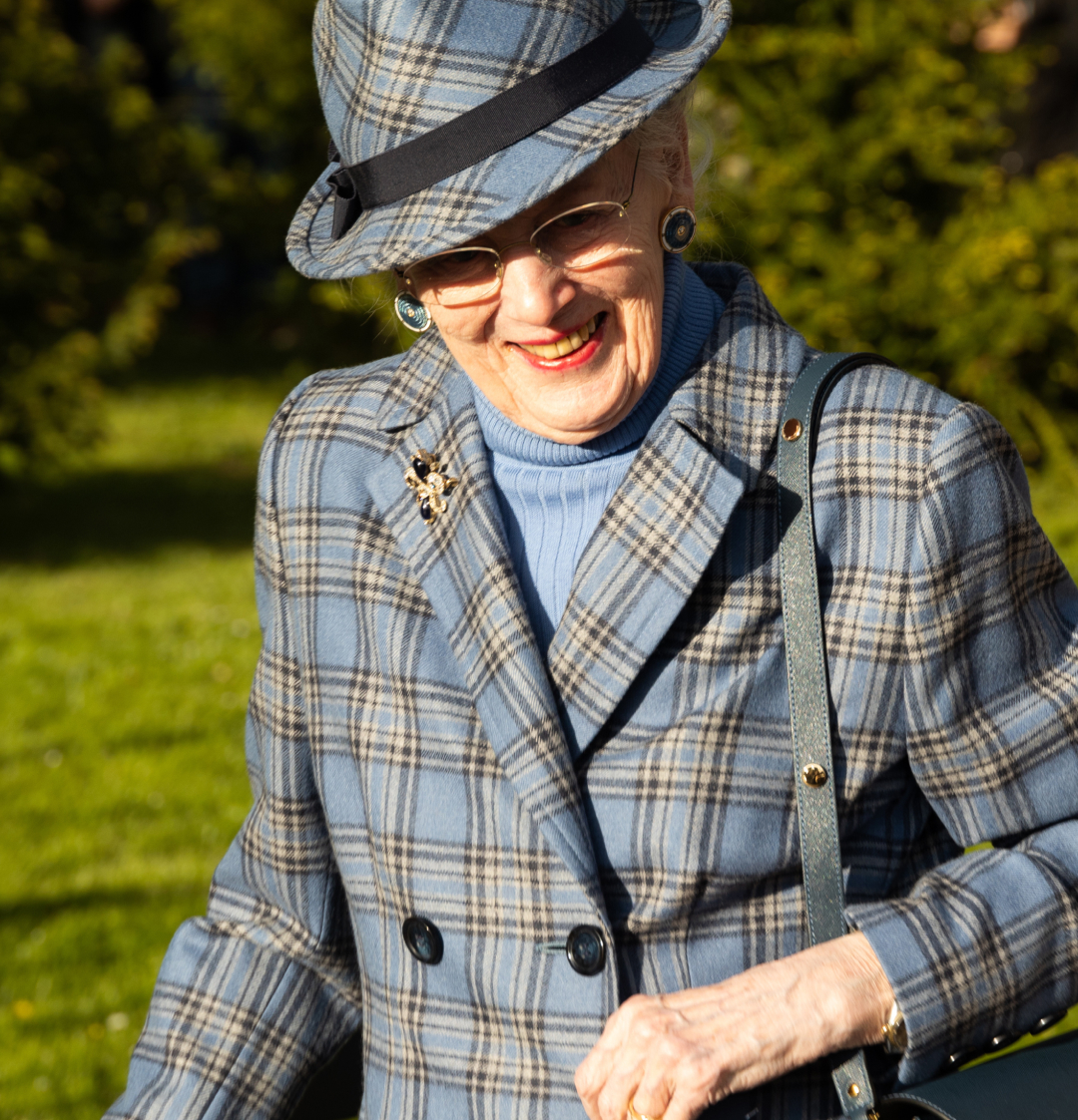 Queen Margrethe wearing a blue plaid coat and matching hat smiling
