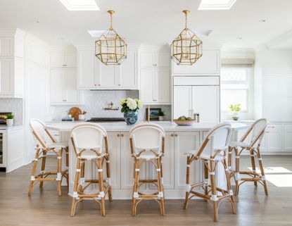 white kitchen with white and wooden bar chairs around a large island with brass pendant lights