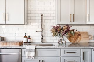 white and gray kitchen with white metro tile backsplash and white wall cabinets, pale gray painted base units, chrome tap, marble countertop