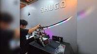 A tech journalist places an RGB samurai sword back onto a pedestal that is actually a PC. The words 'Shugo' can be seen on the wall behind the exhibition piece from Corsair.