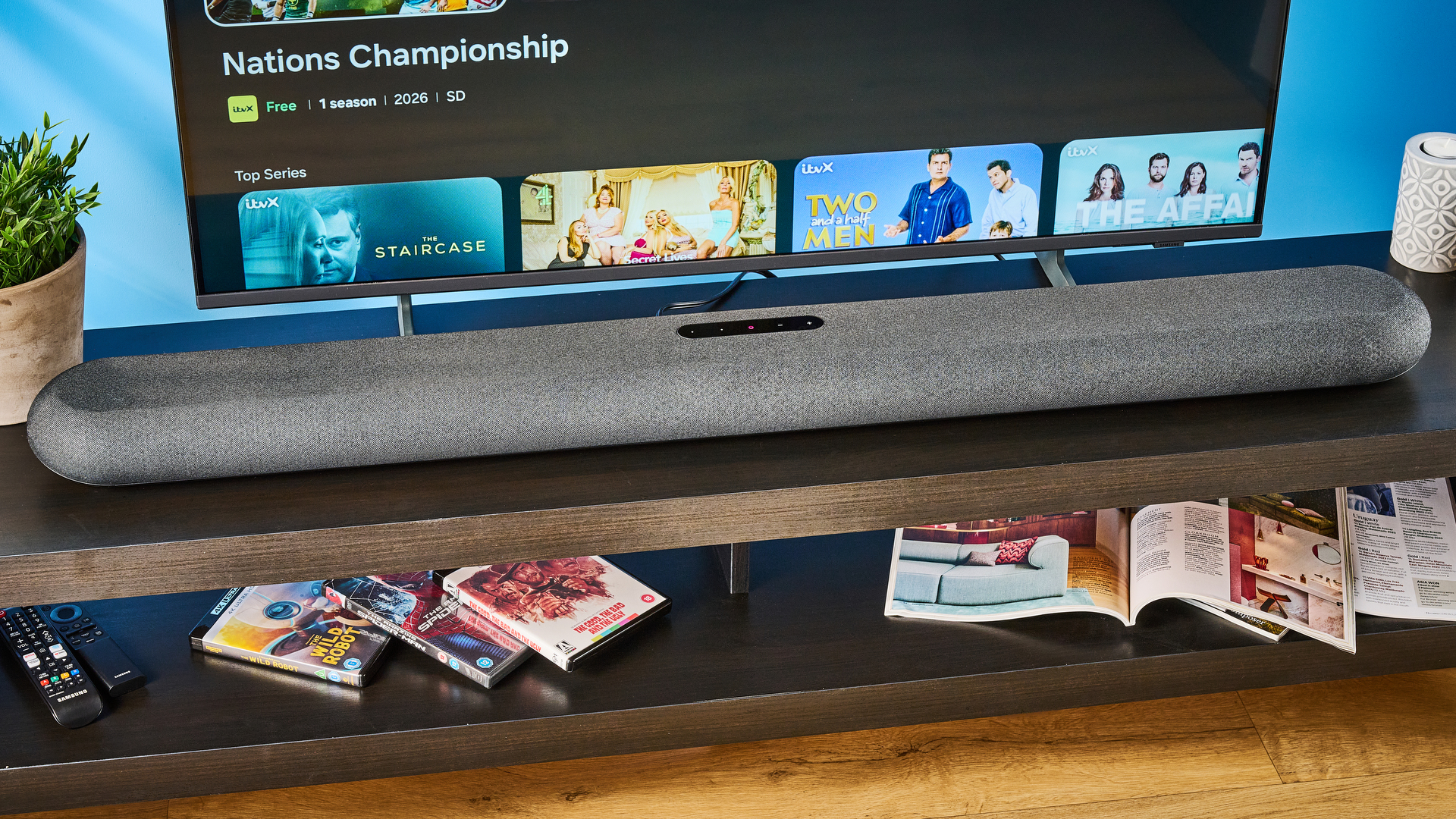 the bluesound pulse cinema soundbar photographed with a TV and the tom's guide blue background