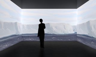 A visitors watches three screens with projection of ice landscape from Antarctica, part of the Antarctic pavilion at London Design Biennale