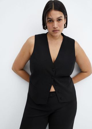 model wears black waist coat and black trousers with hands tucked beehind her back