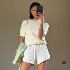 Influencer @smythsisters takes a mirror selfie inside, wearing green Dries Van Noten trainers with Light grey track shorts and a butter yellow short sleeve knit.