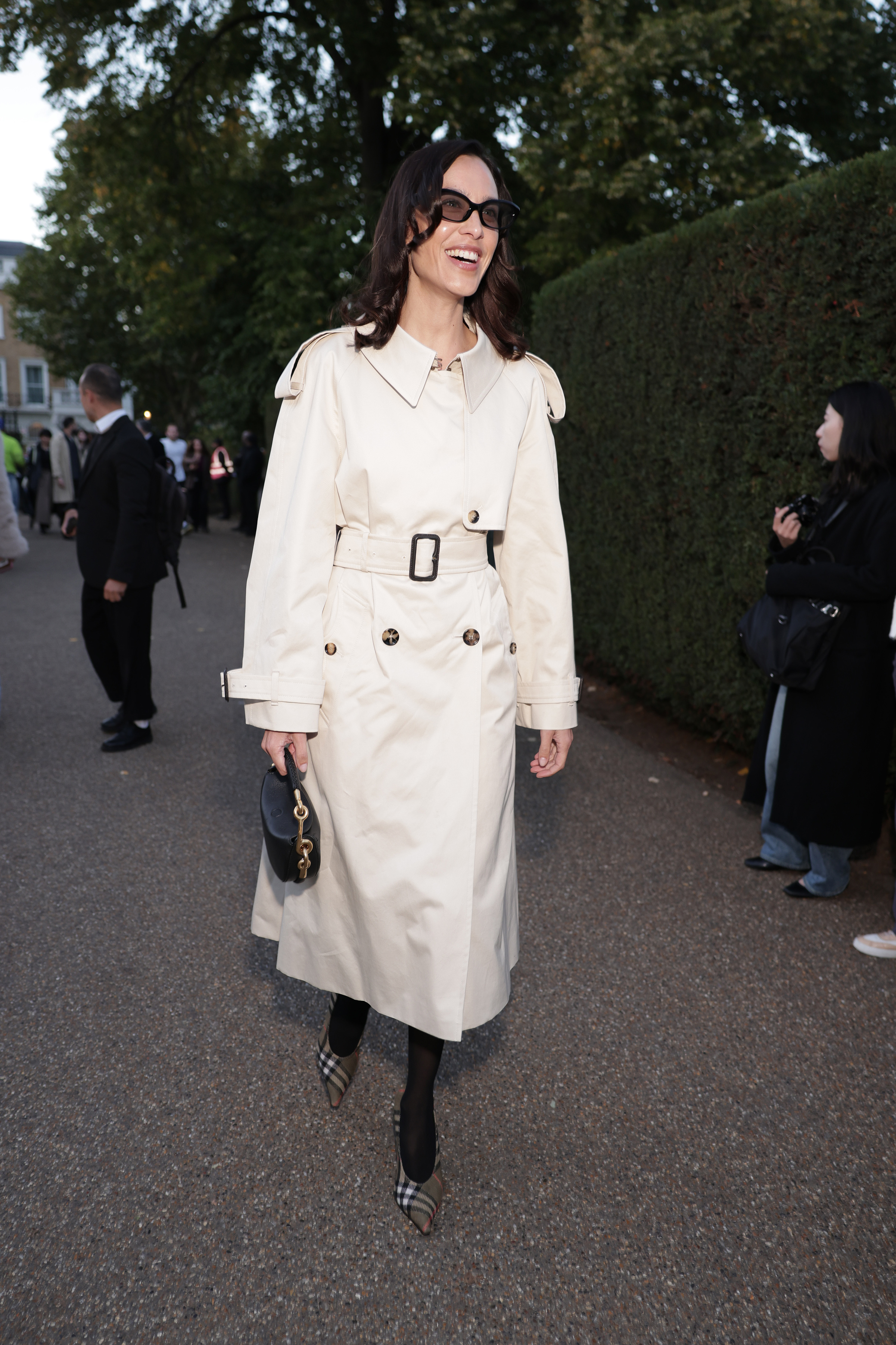 Alexa Chung wears a cream trench coat over semi-sheer tights and checked pointed-toe heels.