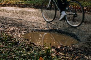 Image shows a rider avoiding potholes while cycling in the rain.