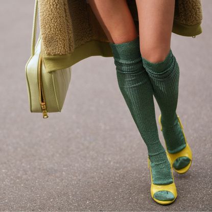 A closeup of a woman's legs wearing knee-high green socks in peep-toe green shoes holding a green bag