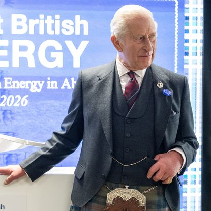 King Charles wearing a gray suit jacket and red tie with a kilt