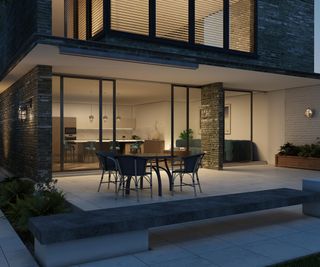 A patio on a contemporary self build with bifold doors leading into the kitchen and outdoor wall lights