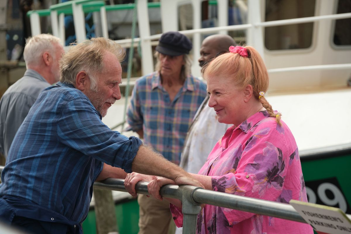 Beyond Paradise season 2 episode 3: Jaime (Danny Webb) and Margo (Felicity Montagu) stand on either side of a railing at the harbour, looking into each other&#039;s eyes. Margo is smiling.