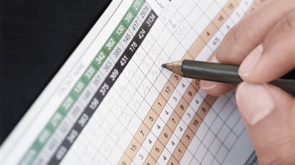 A close up of a golfer filling out a scorecard in pencil