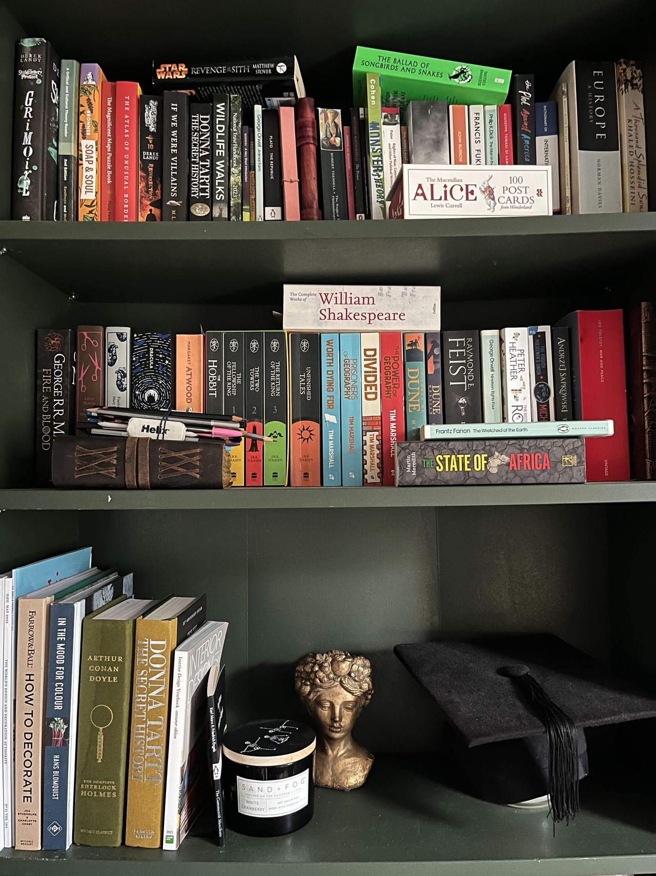 A dark green painted bookshelf with lots of books on it, disorganzied