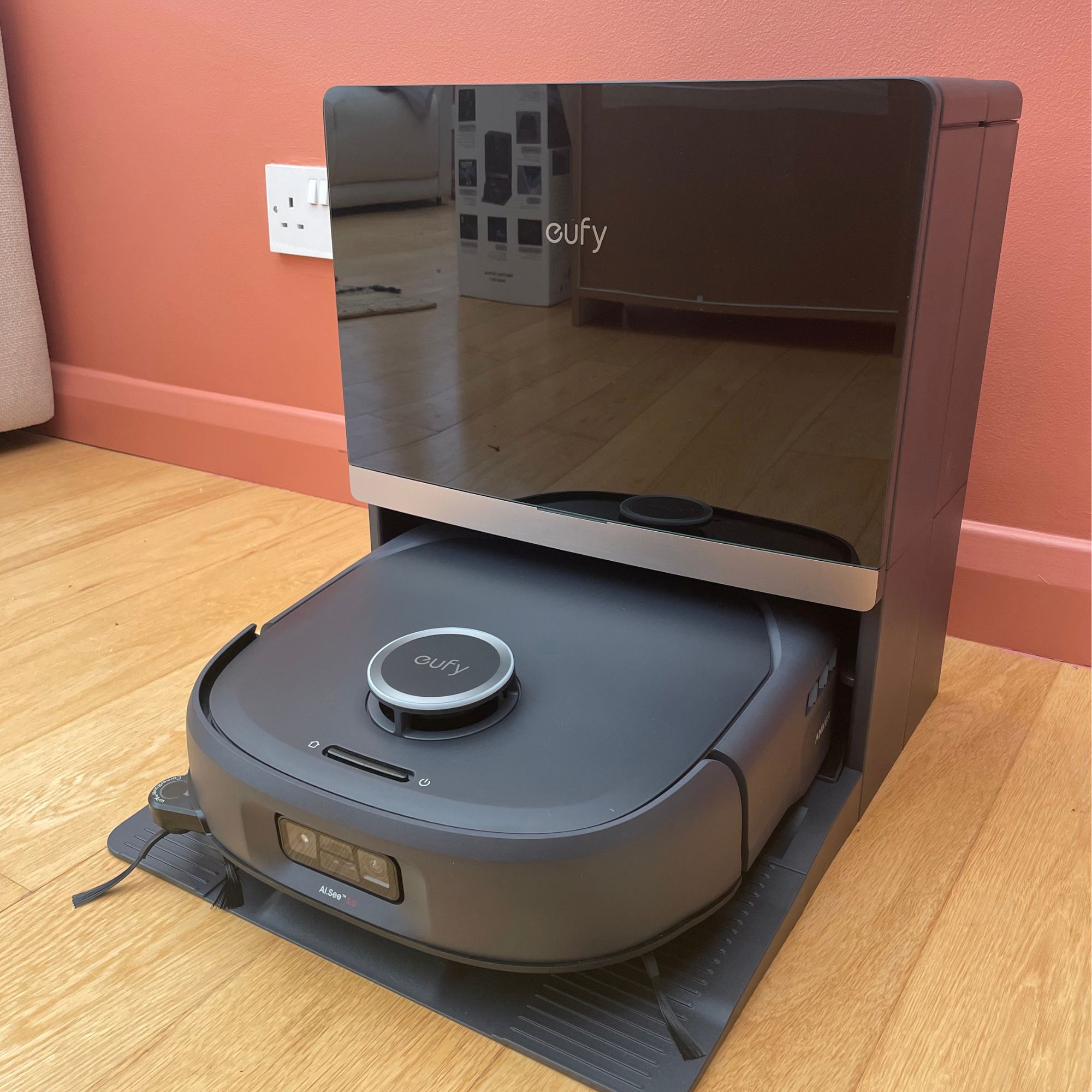 Anker eufy Robot Vacuum E35 Omni and docking station sitting on wood floor in front of a pink painted wall