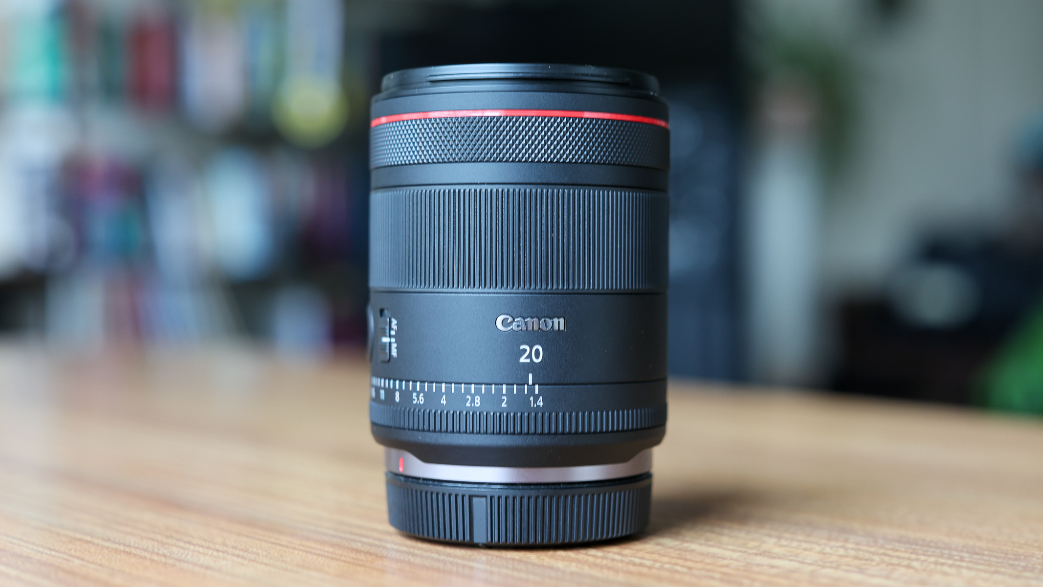 A side view of the Canon RF 20mm f/1.4 L VCM lens on a wooden table.