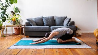 Man performing child's pose yoga move in home