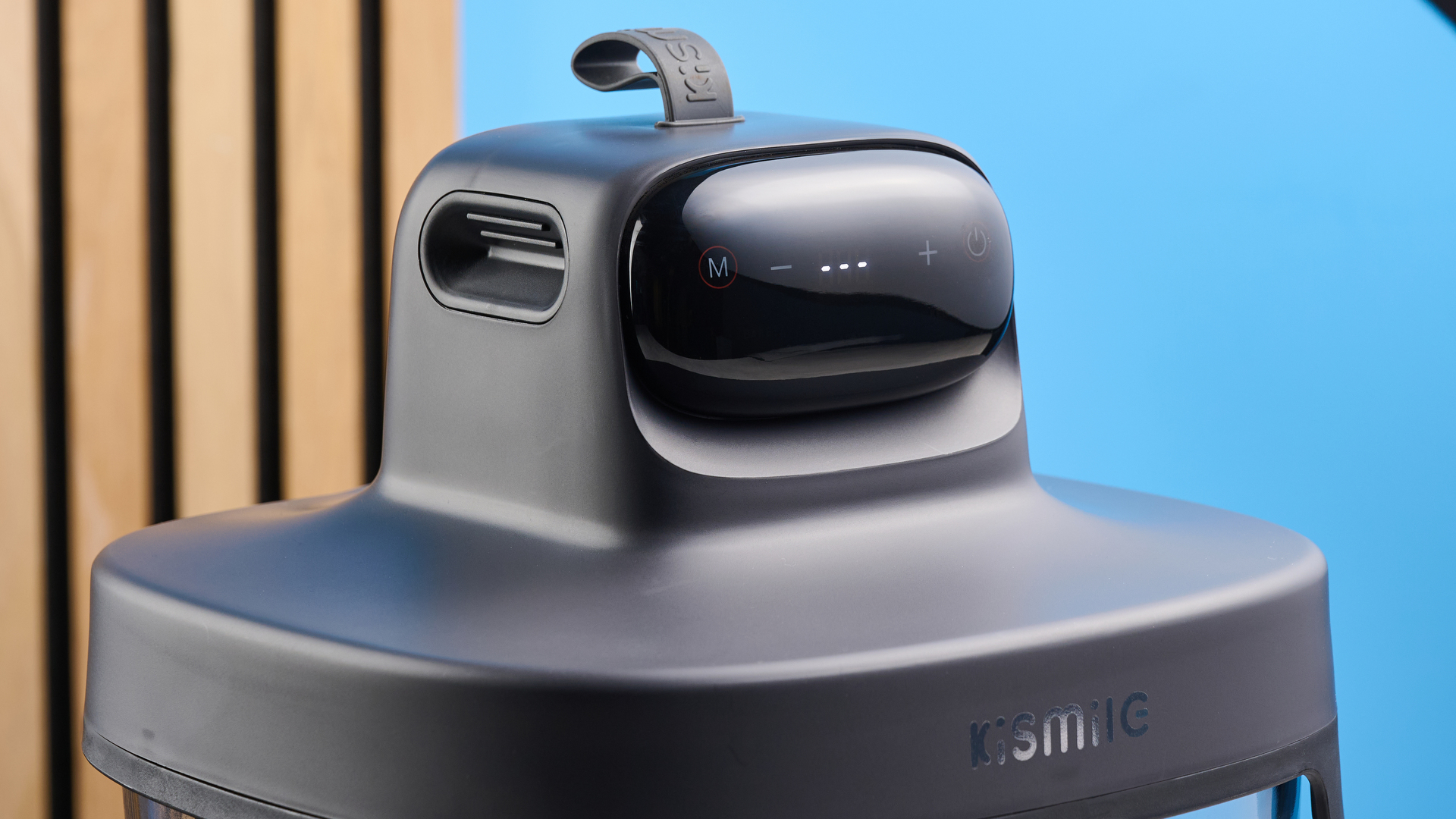 the kismile roasti air fryer with a glass cooking container photographed against a blue and wood background, showing the heating element lid