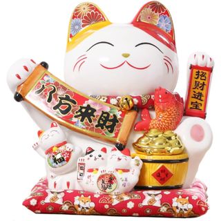 A white heavily decorated Maneki Neko with red decorations, flowers, three smaller cats, and a pot of gold on a red patterned cushion