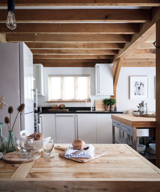 Small kitchen with wooden beams, countertops, cabinetry, window in background.