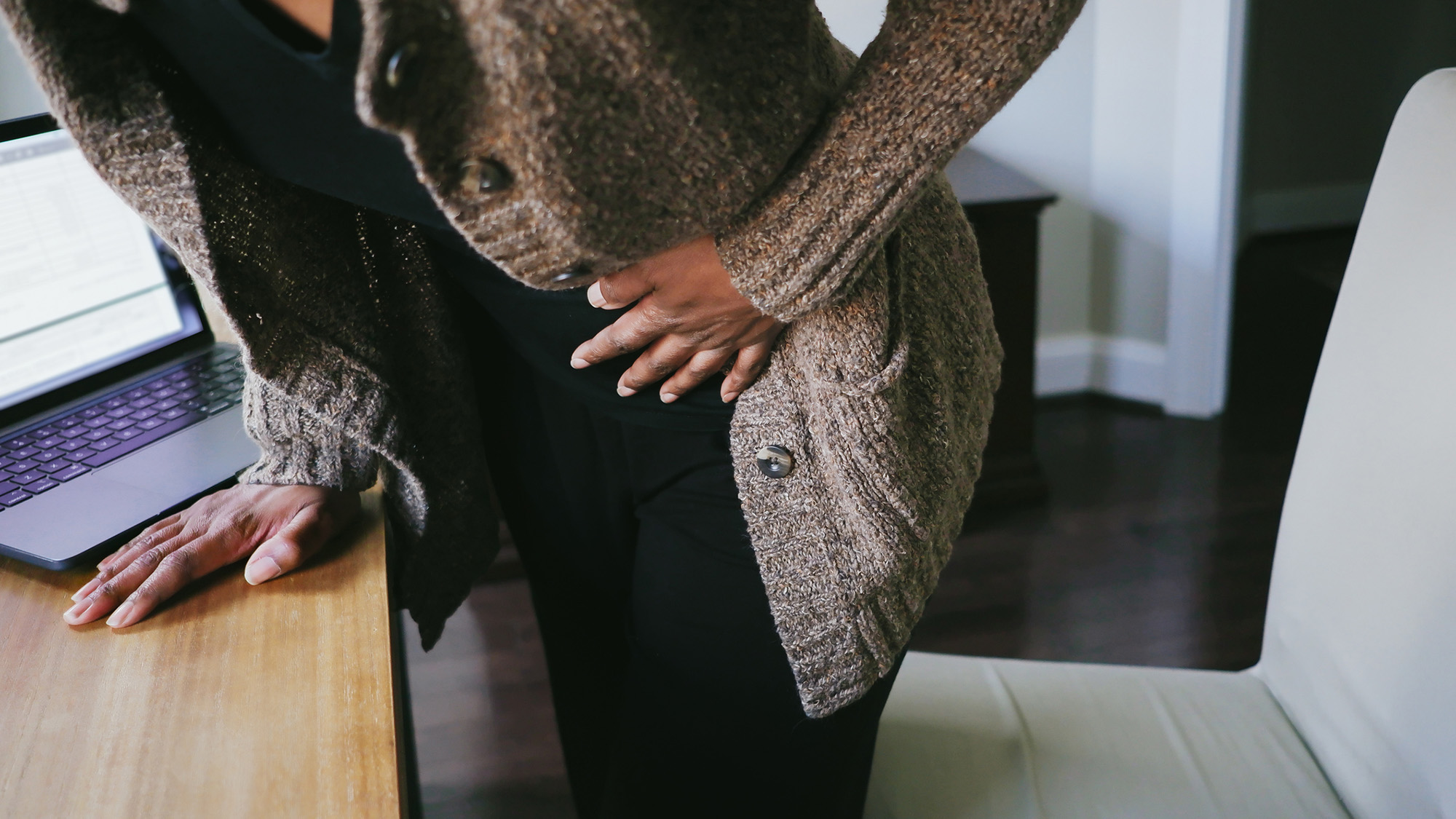 A woman wearing black and a brown sweater clutches her abdomen