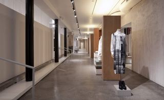 A hallway with doorways along one side and clothing on mannequins and wooden pillars along the other side.