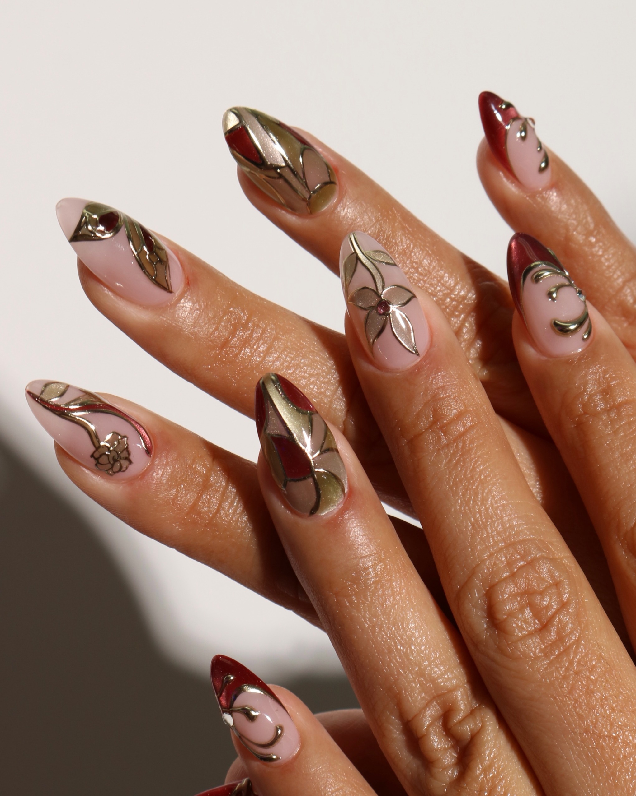 Long almond nails with brown and burgundy sections, fine metallic outlines forming stained glass designs