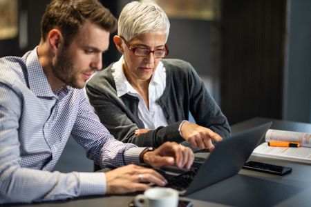 Senior businesswoman cooperating with her male colleague while working on a computer in the office.