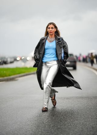 A guest wears a silver fringed long and large necklace, a blue ribbed tank-top from Loewe, a black shiny leather long coat, silver shiny leather flared pants, black mesh / fishnet ballerinas