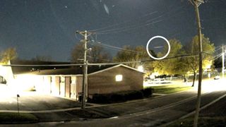 a streak of fire is visible in the night sky above the rooflines of houses in a residential neighborhood