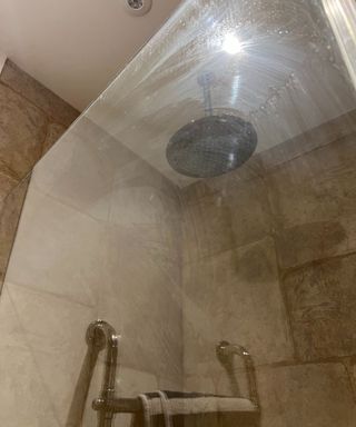 A foggy shower screen with overhead showerhead and brown tiles