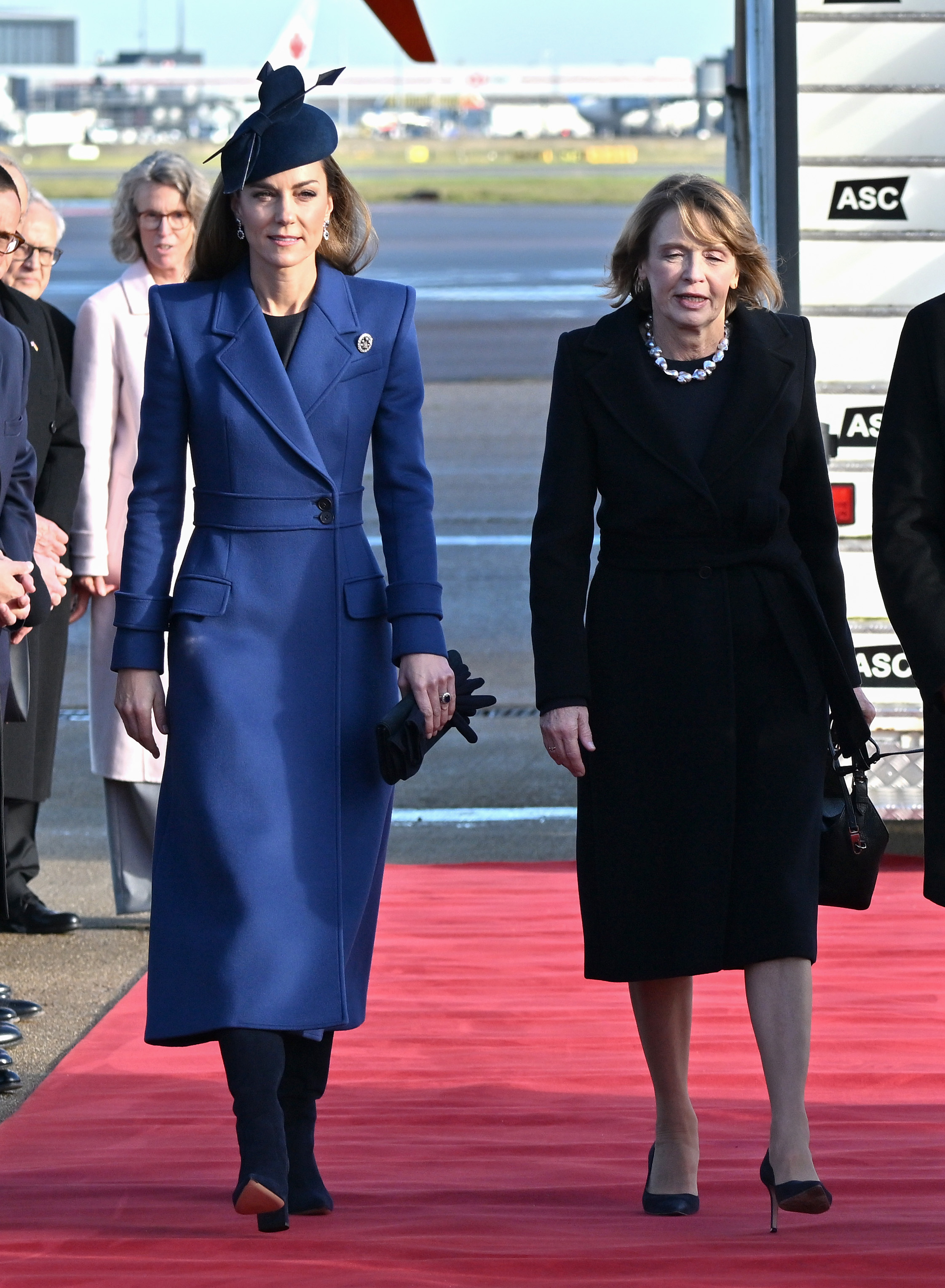 Kate Middleton wears a navy coat with navy suede boots and a navy fascinator.
