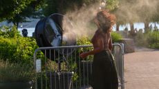 A woman tries to cool off with a fan that spray water to refresh people during a hot day in New York