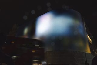 A projection on the Picadilly Circus arcade shows an abstract, cloud-like swathe of blue, purple, and green.