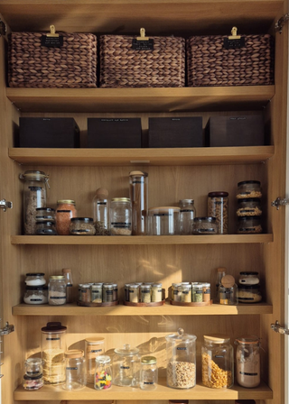 A pantry cabinet with glass jars and wicker baskets