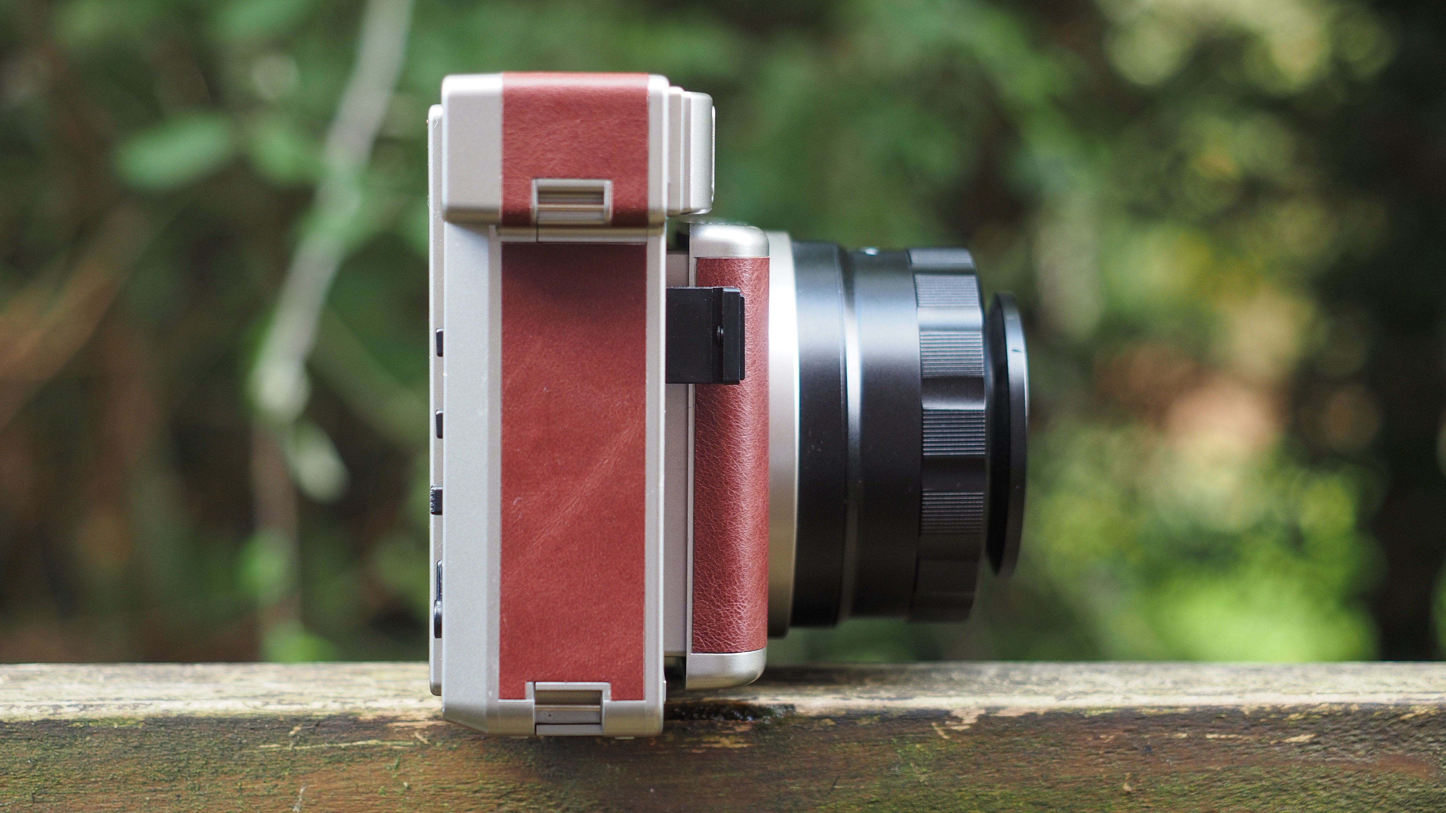 Lomo'Instant Wide Glass camera, sitting on a wooden surface, outdoors against a wooded background